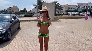 Nahá Monika Fox se prochází po molu v klobouku a ukazuje velké prsa